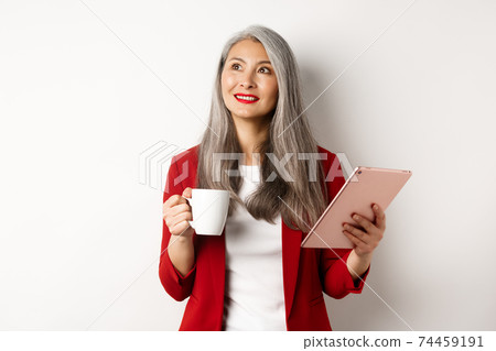 Business people concept. Asian businesswoman drinking coffee and holding digital tablet, smiling thoughtful at upper left corner, white background Business people concept. Asian businesswoman drinking coffee and holding digital tablet, smiling thoughtful at upper left corner, white background 74459191