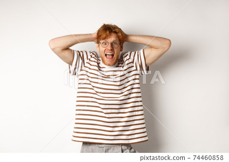 Frustrated redhead man panicking, screaming and holding hands on head, standing on white background Frustrated redhead man panicking, screaming and holding hands on head, standing on white background 74460858