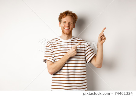 Handsome redhead man showing logo, pointing fingers right and smiling, standing over white background Handsome redhead man showing logo, pointing fingers right and smiling, standing over white background 74461324