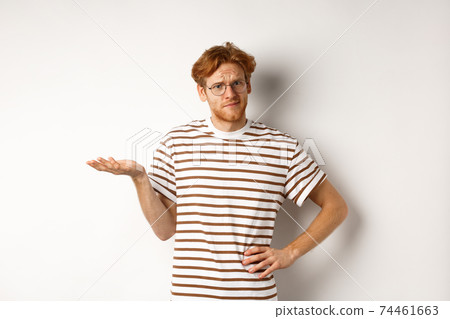 So what. Confused and annoyed redhead man waiting for reply, standing questioned with raised hand, holding something on palm, white background So what. Confused and annoyed redhead man waiting for reply, standing questioned with raised hand, holding something on palm, white background 74461663