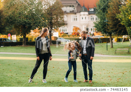 A happy family of three runs through the grass in Austria's old town.A family walks through a small town in Austria.Europe.Velden am werten Zee 74463145