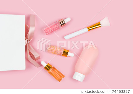 Skin care essence glass bottles and body lotion in plastic container with paper gift shopping bag on pink background. Hydrating anti aging serum, collagen and peptides, bottle with dropper. Cosmetics Skin care essence glass bottles and body lotion in plastic container with paper gift shopping bag on pink background. Hydrating anti aging serum, collagen and peptides, bottle with dropper. Cosmetics 74463237