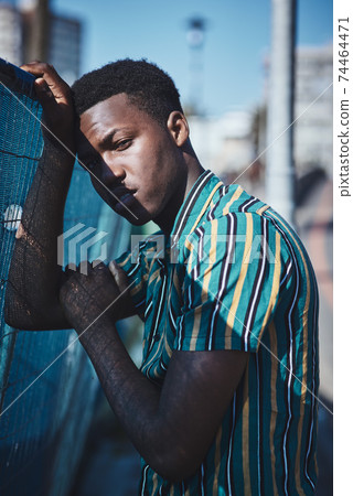 A portrait of a young African man leaning against a fence. A portrait of a young African man leaning against a fence. 74464471