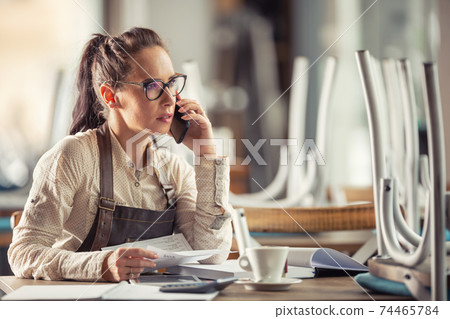 Restaurant owner consults bookeeping with her accountant sitting over paperwork with a coffee Restaurant owner consults bookeeping with her accountant sitting over paperwork with a coffee 74465784