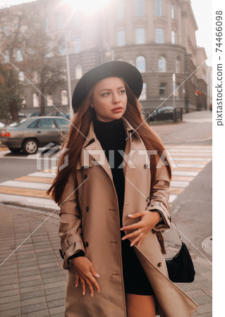 Stylish young woman in a beige coat in a black hat on a city street. Women's street fashion. Autumn clothing.Urban style Stylish young woman in a beige coat in a black hat on a city street. Women's street fashion. Autumn clothing.Urban style 74466098