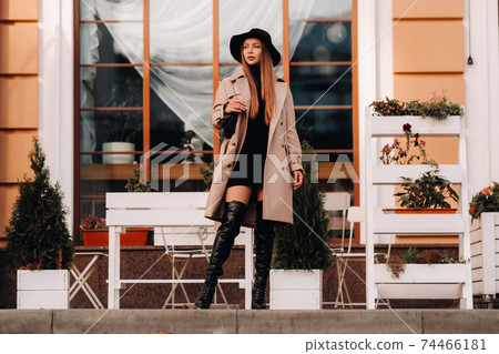 Stylish young woman in a beige coat in a black hat on a city street. Women's street fashion. Autumn clothing.Urban style 74466181