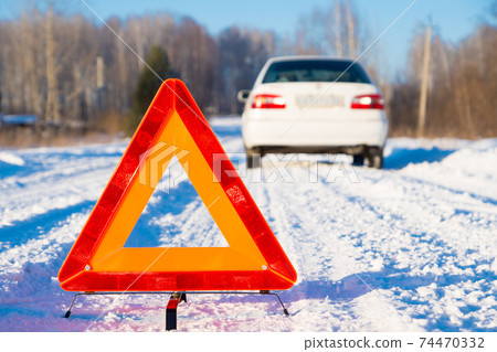 warning triangle and white car on winter snowy country road, focus on triangle warning triangle and white car on winter snowy country road, focus on triangle 74470332