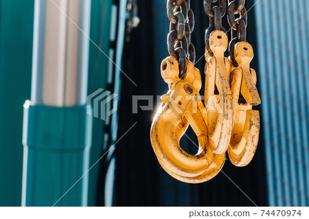 The hooks of the mobile crane near the glass of high buildings.Lots of hooks hanging from chains suspended from a crane 74470974