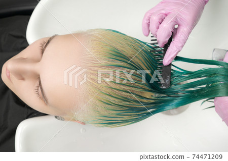 Top view of hairstylist holds wet hair in hand and combs long green and discolored hair of client while washing hair in shower in special sink Top view of hairstylist holds wet hair in hand and combs long green and discolored hair of client while washing hair in shower in special sink 74471209
