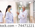 Caucasian senior male doctor wearing medical protective mask discussing of patient treatment case with female doctor at hospital corridor during Coronavirus epidemic 74471221