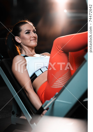 Young woman practicing legs on the machine in a gym Young woman practicing legs on the machine in a gym 74472642