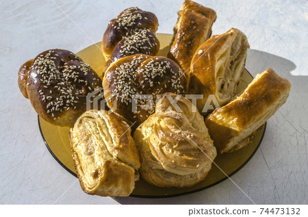 Ceramic plate on the old kitchen table with the Gata, Eclair and rolls covered with sesame seeds Ceramic plate on the old kitchen table with the Gata, Eclair and rolls covered with sesame seeds 74473132