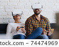 Young Couple Playing Virtual Reality With Headset On Sofa 74474969