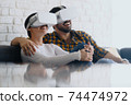 Young Couple Playing Virtual Reality With Headset On Sofa 74474972