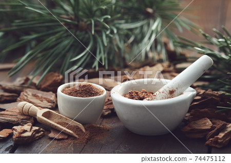 Mortars of powdered pine bark, dry pine bark on wooden board. Branches of pine tree on background. Mortars of powdered pine bark, dry pine bark on wooden board. Branches of pine tree on background. 74475112