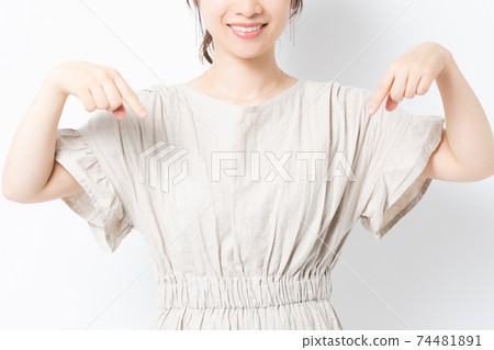 Young woman standing in front of a white wall and pointing to a point Young woman standing in front of a white wall and pointing to a point 74481891