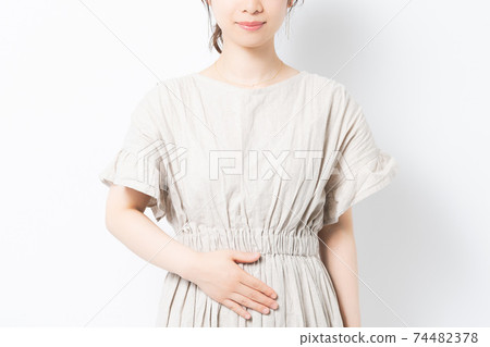 A young woman standing in front of a white background and putting her hands on her belly 74482378
