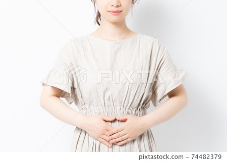 A young woman standing in front of a white background and putting her hands on her belly A young woman standing in front of a white background and putting her hands on her belly 74482379