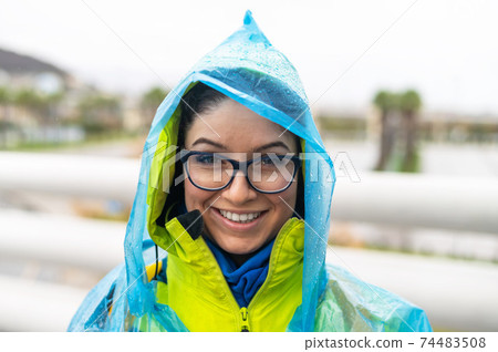 Portrait of a smiling woman with glasses wearing a raincoat outdoors. 74483508