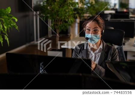 Portrait of a female operator Call Center wearing a medical mask for the desktop Portrait of a female operator Call Center wearing a medical mask for the desktop 74483556