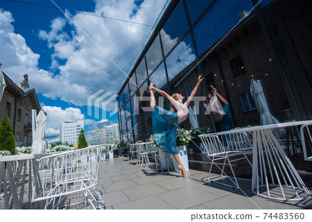 A beautiful ballerina is dancing outdoors on a warm summer day. Young flexible woman in pointe shoes and ballet tutu posing in a street cafe A beautiful ballerina is dancing outdoors on a warm summer day. Young flexible woman in pointe shoes and ballet tutu posing in a street cafe 74483560