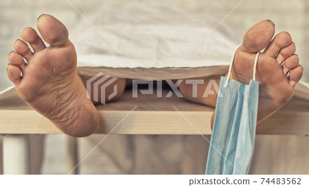 Close-up of dead men feet in a morgue with a medical mask on a toe. An unrecognizable woman has died from the coronavirus Close-up of dead men feet in a morgue with a medical mask on a toe. An unrecognizable woman has died from the coronavirus 74483562