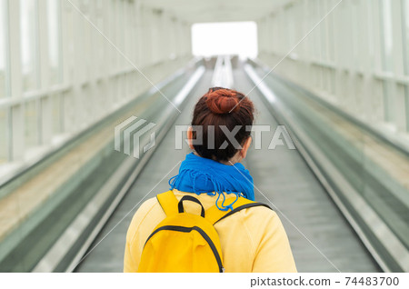 Back view of woman with backpack moving on escalator. 74483700
