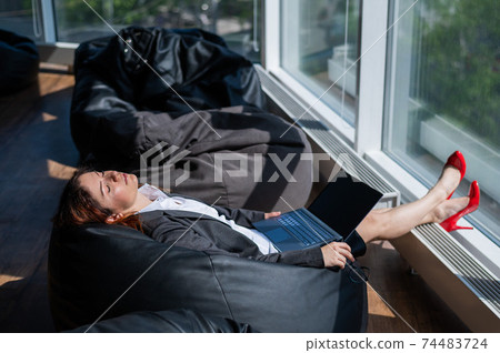 Business lady sleeps sitting in a modern office comfortable bob chair bag. A woman in a suit fell asleep at work on a laptop. Caring for the convenience and comfort of employees. Business lady sleeps sitting in a modern office comfortable bob chair bag. A woman in a suit fell asleep at work on a laptop. Caring for the convenience and comfort of employees. 74483724
