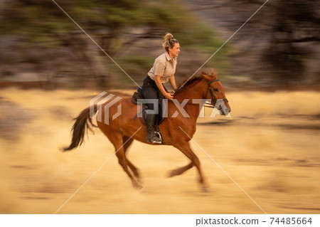 Slow pan of blonde riding through savannah 74485664