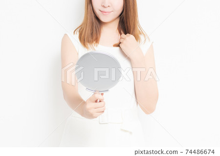 Young woman looking in a hand mirror in front of a white background Young woman looking in a hand mirror in front of a white background 74486674