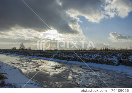 Frozen small river with ice floe and clouds with sunshine on the sky 74489066