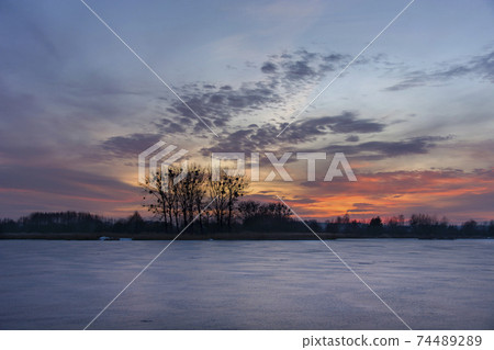 Frozen lake, trees and colorful evening sky Frozen lake, trees and colorful evening sky 74489289