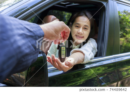 Close up of dealer giving key to new owner car. New car. Auto dealer giving woman automobile key for test drive on country road. Soft focus smiling women try to test drive a car on road with dealer. Close up of dealer giving key to new owner car. New car. Auto dealer giving woman automobile key for test drive on country road. Soft focus smiling women try to test drive a car on road with dealer. 74489642