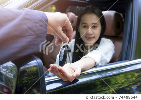Close up of dealer giving key to new owner car. New car. Auto dealer giving woman automobile key for test drive on country road. Soft focus smiling women try to test drive a car on road with dealer. Close up of dealer giving key to new owner car. New car. Auto dealer giving woman automobile key for test drive on country road. Soft focus smiling women try to test drive a car on road with dealer. 74489644