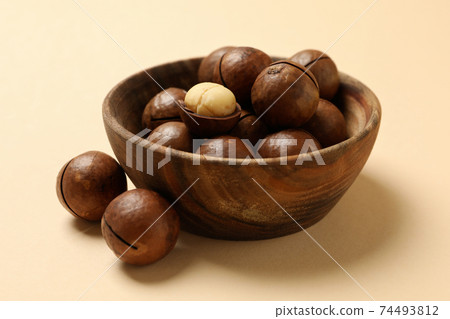 Bowl with tasty macadamia nuts on beige background Bowl with tasty macadamia nuts on beige background 74493812