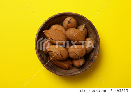 Bowl with tasty pecan nuts on yellow background 74493815
