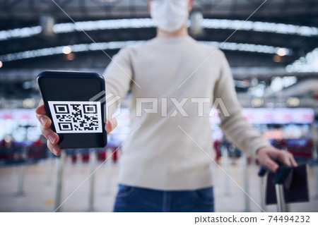 Man wearing face mask and holding smart phone with QR code at airport Man wearing face mask and holding smart phone with QR code at airport 74494232