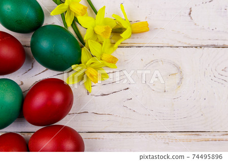 Painted Easter eggs and yellow daffodils on white wooden background. Easter composition. Top view, copy space Painted Easter eggs and yellow daffodils on white wooden background. Easter composition. Top view, copy space 74495896