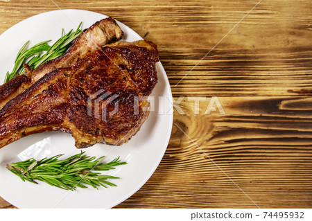 Roasted beef rib eye steak on bone with rosemary in white plate on wooden table Roasted beef rib eye steak on bone with rosemary in white plate on wooden table 74495932