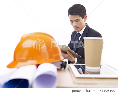 young asian executive working in office with blueprints and safety hat young asian executive working in office with blueprints and safety hat 74496499