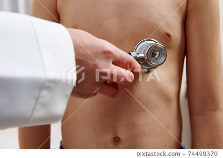 Pediatrician listens to a patient with a stethoscope. Auscultation of lungs and heart in pediatric practice and regular chek-up concept. Closeup 74499370