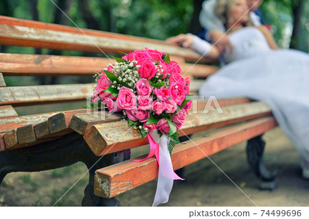 bouquet on wooden bench with bride and groom in the background, focus on the flowers bouquet on wooden bench with bride and groom in the background, focus on the flowers 74499696