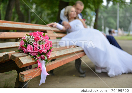 bouquet on wooden bench with bride and groom in the background, focus on the flowers 74499700