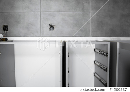 Stainless telescopic bayonet drawer slide guides, installed on a kitchen cabinet from gray chipboard. Accessories for carpentry used in the construction of furniture. Custom kitchen installation. 74500287