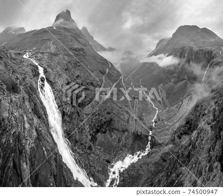 Grayscale. Summer Trollstigen serpentine mountain path road and Stigfossen waterfall view from The Trolls Path Viewpoint, Norway. 74500947