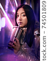 Young adult trendy woman in glowing neon light drinking beverage 74501809
