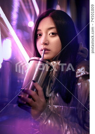 Young adult trendy woman in glowing neon light drinking beverage Young adult trendy woman in glowing neon light drinking beverage 74501809
