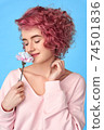 Smiling girl with pink curly hair and nose piercing sniffing carnation flower and enjoying fragrance 74501836