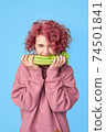Pretty girl with pink curly hair in pink casual hoodie biting bunch of fresh celery 74501841