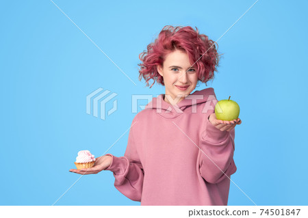 Girl in hoodie preferring fresh green apple to sweet cupcake 74501847